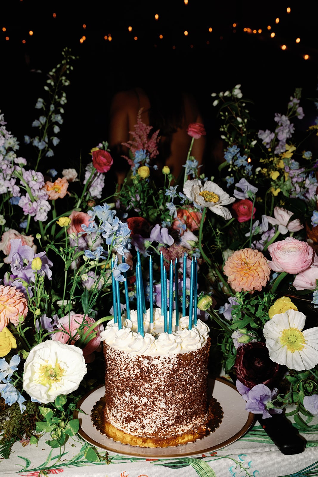 Vibrant florals surround a festive birthday cake with candles atop a custom table linen at a luxury wedding.