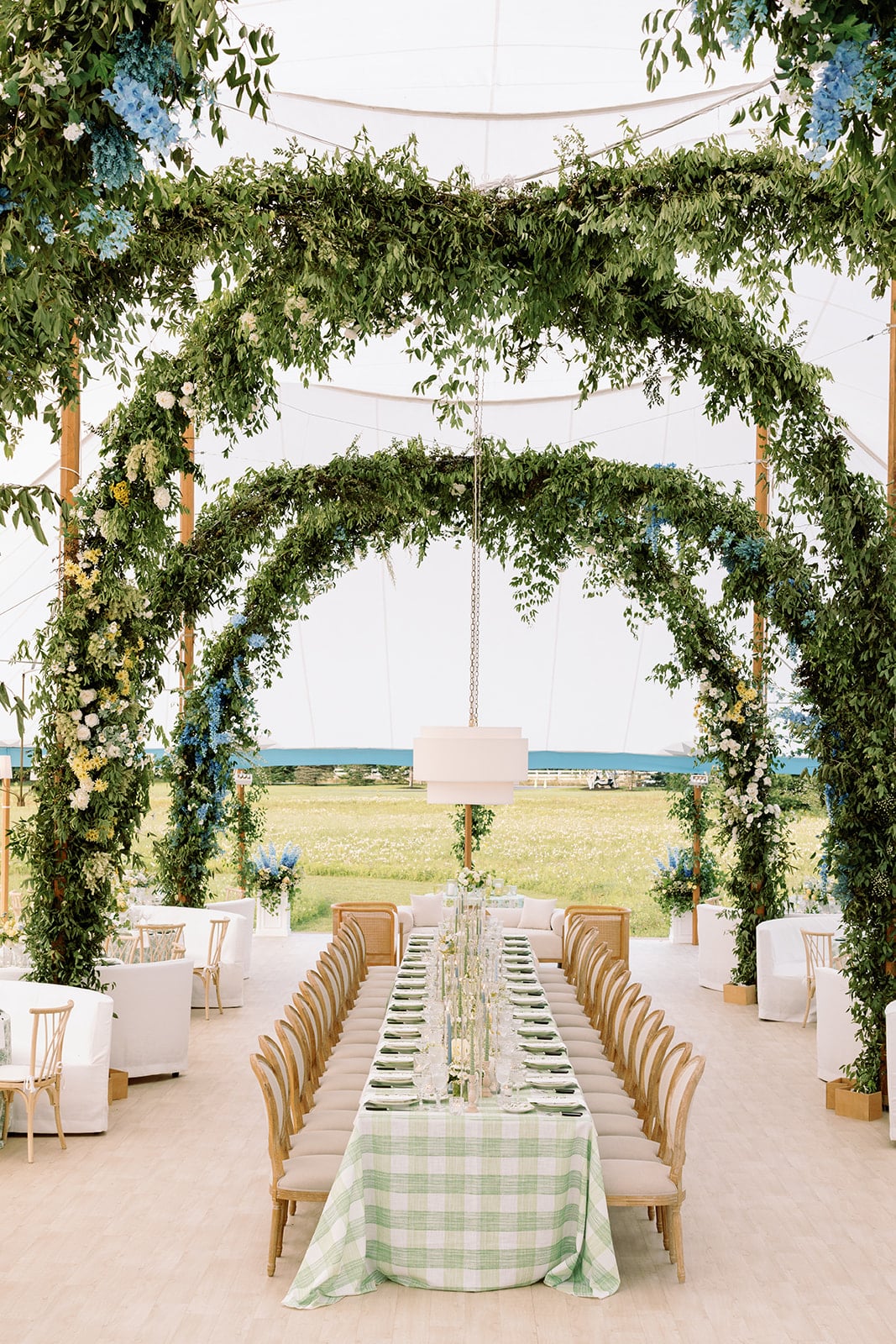 Grand floral arches criss-cross a dinner table set with custom linens at an estate wedding at a private home in New Hampshire.